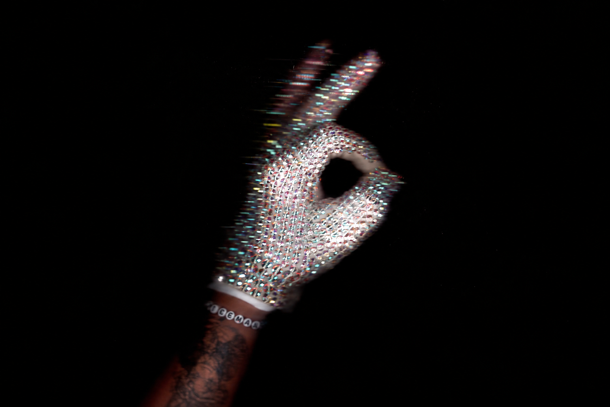 A rhinestone-covered glove making an OK gesture against a black background.